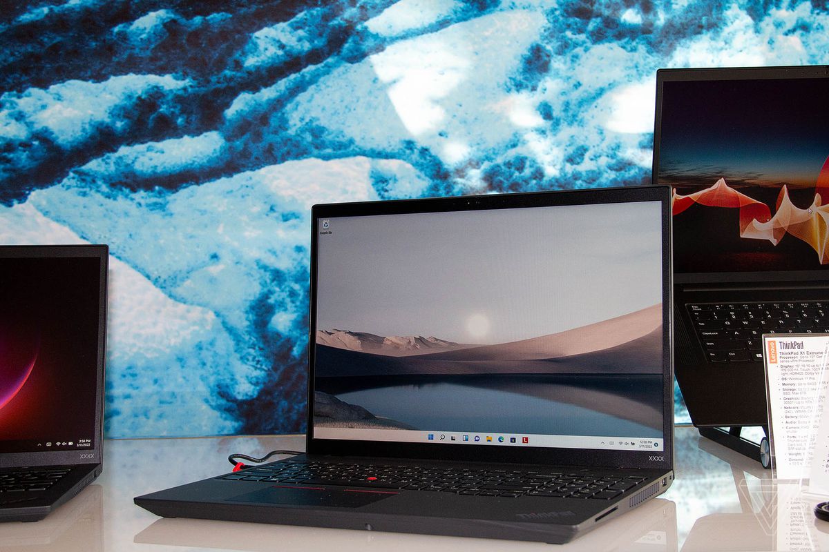Lenovo ThinkPad T16 sobre una mesa blanca abierta, inclinada hacia la izquierda.  La pantalla muestra una cadena montañosa al otro lado de un lago.