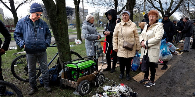 Los residentes locales se reúnen cerca de un generador para cargar sus dispositivos móviles en un área controlada por las fuerzas separatistas respaldadas por Rusia en Mariupol, Ucrania, el viernes 22 de abril de 2022 (AP Photo/Alexei Alexandrov)