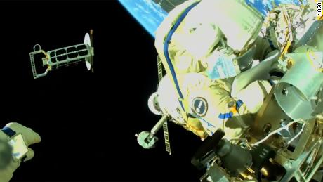 Se puede ver a Cristoforetti trabajando en el exterior de la Estación Espacial Internacional mientras Artemyev, cuya mano se muestra en la parte inferior izquierda, lanza un nanosatélite a la órbita. 