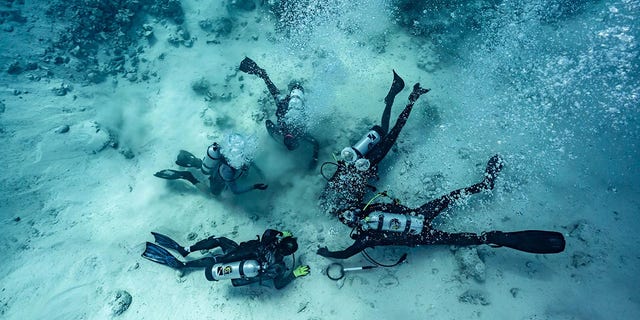 Se muestra a los buzos excavando en busca de un tesoro enterrado en el fondo del mar, el lugar de un naufragio en las Bahamas.