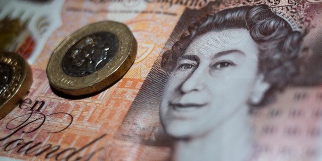 Moneda británica de dos libras colocada encima de un billete del Banco de Inglaterra de 10 libras con el retrato de la reina Isabel II.