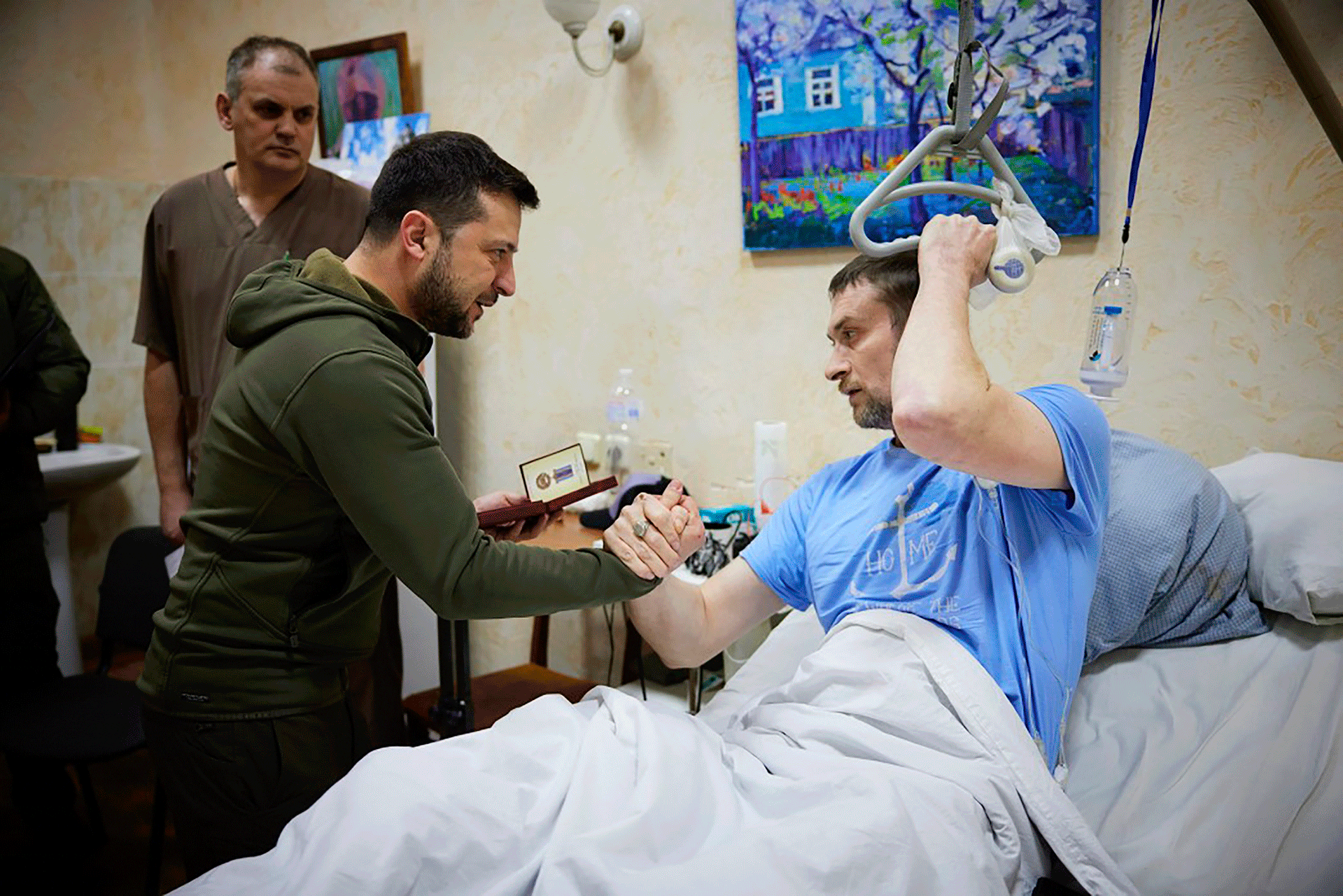 En esta foto proporcionada por la Oficina de Prensa Presidencial de Ucrania el domingo 13 de marzo de 2022, el presidente Volodymyr Zelensky, en el centro, le da la mano a un soldado herido mientras visita un hospital en Kyiv, Ucrania.