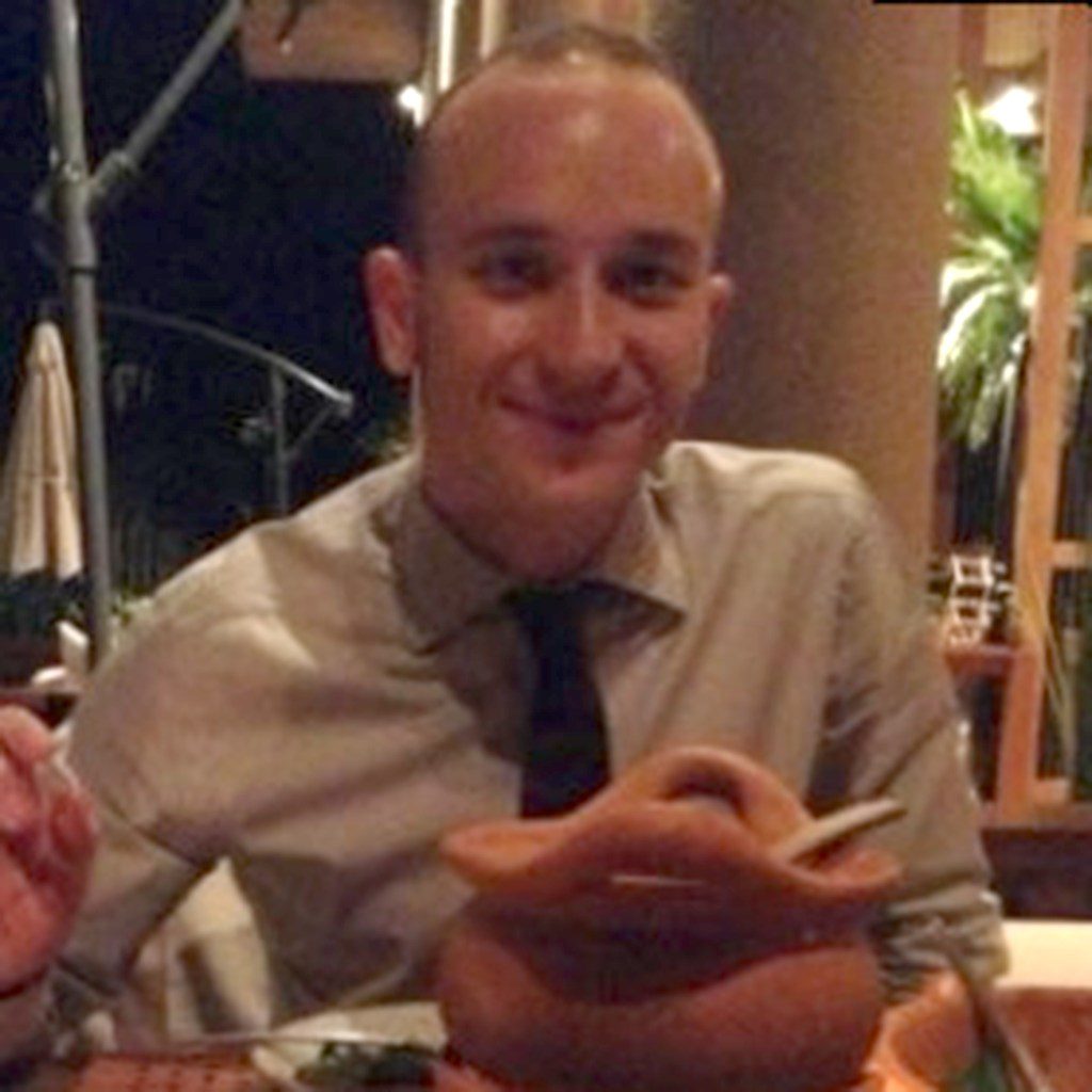 Marco Bellolini, vestido con camisa y corbata, sonríe en una sincera foto tomada en una mesa de un restaurante.