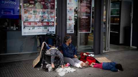 Una mujer sin hogar pide limosna afuera de un supermercado con sus hijas en Buenos Aires.