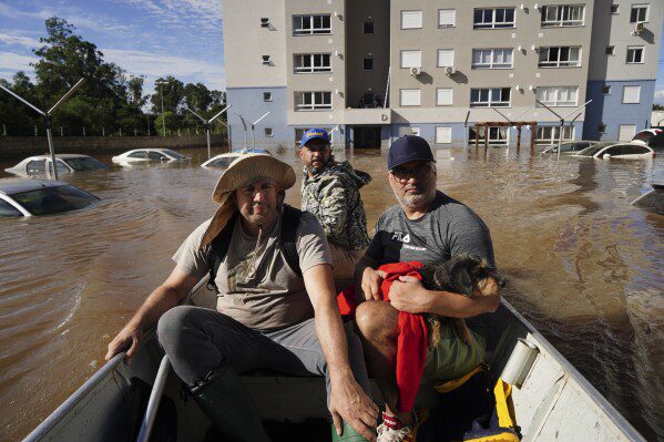 La gente rescata a una perra llamada Maya de un área inundada después de fuertes lluvias en Canoas, estado de Rio Grande do Sul, Brasil, el jueves 9 de mayo de 2024. (Foto AP/Carlos Macedo)